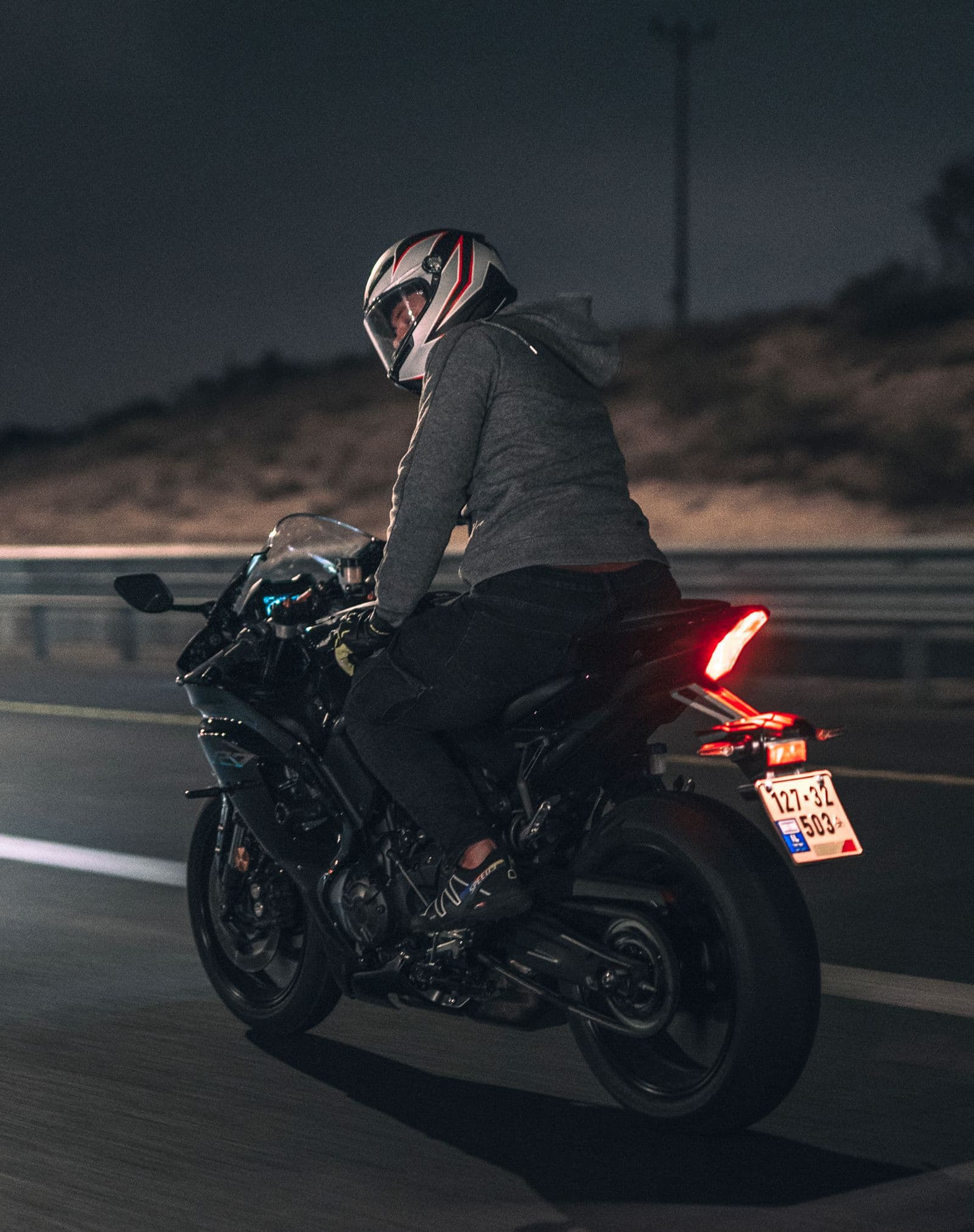 A rider on a sportsbike at night, tail light glowing red on an empty highway